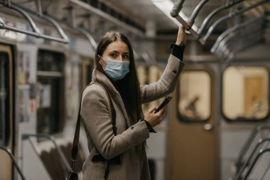 Coronavirus 'un yayılmasını önlemek için tıbbi maske takan bir kadın metro vagonuna bakıyor. Yüzünde COVID-19 maskesi olan bir kız trende cep telefonuyla poz veriyor..
