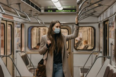 Coronavirus 'un yayılmasını önlemek için maskeli bir kadın metro vagonunun ortasındaki tırabzana tutunuyor. COVID-19 'a karşı cerrahi maskeli güzel bir kız bir metro treninde duruyor..