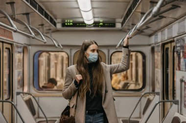 Coronavirus 'un yayılmasını önlemek için maskeli bir kadın metro vagonunun ortasındaki tırabzana tutunuyor. COVID-19 'a karşı cerrahi maskeli bir kız bir metro treninde duruyor..