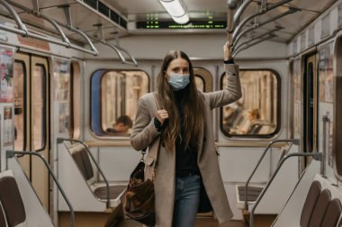 Koronavirüsün yayılmasını önlemek için maske takan bir kadın tırabzana tutunuyor ve metro vagonunun ortasında poz veriyor. COVID-19 'a karşı cerrahi maskeli bir kız bir metro treninde duruyor.