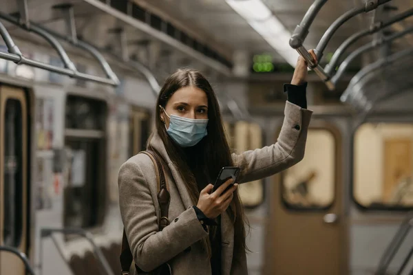 Koronavirüsün yayılmasını önlemek için tıbbi maske takan bir kadın metro vagonunda poz veriyor. Yüzünde COVID-19 maskesi olan bir kız trende cep telefonu tutuyor..