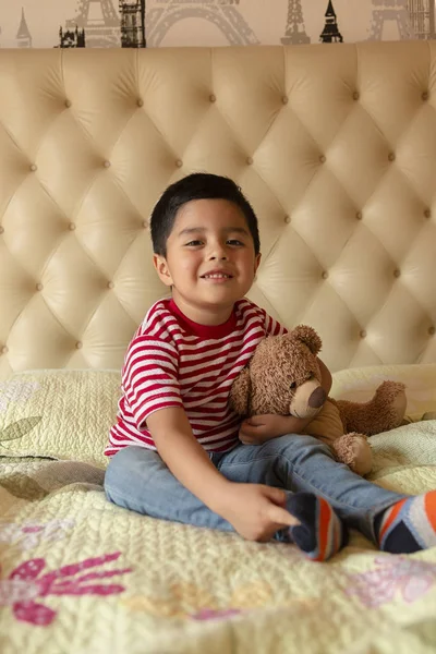 4 year old boy sitting on the bed with his favorite teddy bear smiling at the camera