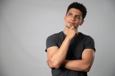 Genç İspanyol bir adam eli çenesinde, bir fikri olan bir adamla stüdyoda gri arka planlı bir portre çiziyor.