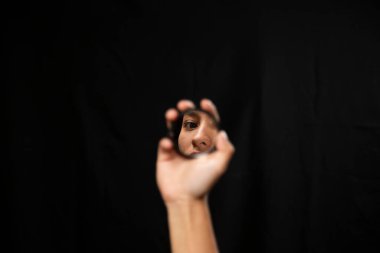 Siyah arka planda aynaya bakan İspanyol bir kadın - küçük bir ayna tutan bir yüz yansıması - odaklanmış yansıma