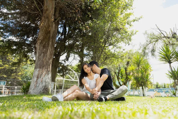 若いヒスパニック系のカップルが草の上に座って楽しんでいます 晴れた日に自然公園を散歩するカップル — ストック写真