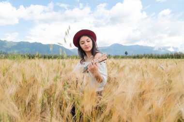 Altın buğday tarlasının ortasında ukulele çalan İspanyol bir sanatçı. Doğadan esinlenerek ukulelesini tutan hippi bir kadın.