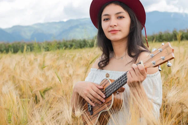 Female artist playing her ukulele in the middle of a golden wheat field - Hipster woman in the middle of a field holding her ukulele - Artist inspired by nature