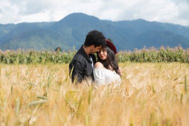 Buğday tarlasının ortasında kucaklaşan genç İspanyol çift, altın buğday tarlasında aşk anının tadını çıkarıyor.