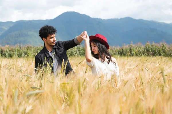 Young couple dancing in love in the middle of a wheat field - Hispanic couple having fun in the summer at sunset - Young man spinning his girlfriend by the hand