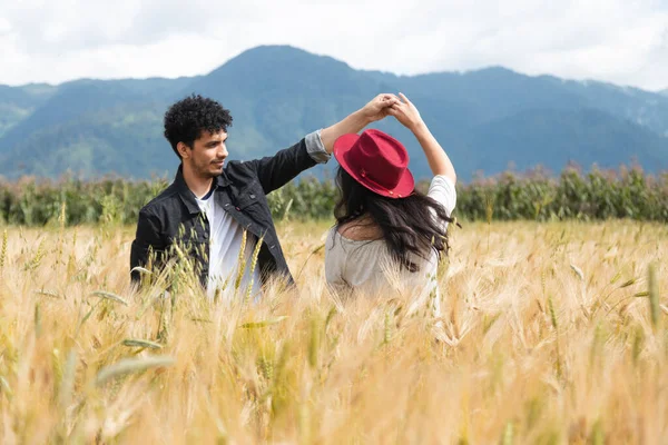 Young couple dancing in love in the middle of a wheat field - Hispanic couple having fun in the summer at sunset - Young man spinning his girlfriend by the hand