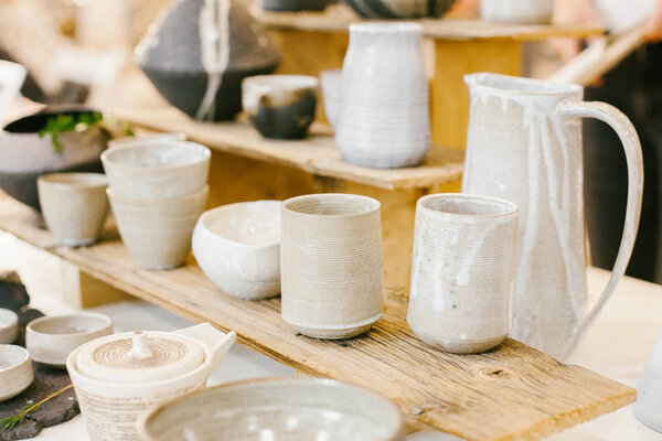 Набор керамических минималистичных ваз и чашек на мягком теплом фоне.