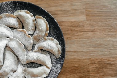 Koyu tabakta ev yapımı hamur tatlısı ve ahşap masa üzerinde un. Ukraynalı vareniki. Kapatın. Üst görünüm.