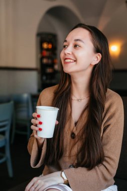 Çekici, güzel bir kızın portresi. Elinde bir fincan kahve tutuyor ve gülümsüyor. Pozitif öğrenci bir kafede dinleniyor, kahvesini içiyor.