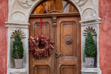Kahverengi, eski, zarif, ahşap kapılı, süs çiçeği çelenkli, saksıda yeşil bitkiler, kırmızı duvar. Cesky Krumlov, Güney Bohemya, Çek Cumhuriyeti, 26 Eylül 2020