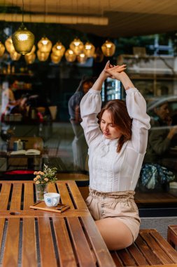 Kafede bir fincan kahve tutan genç ve güzel bir kadın. Tatilde seyahat ederken poz veren kadın blog yazarının açık hava portresi. Mutlu serbest çalışan yeni fikirler düşünüyor.. 