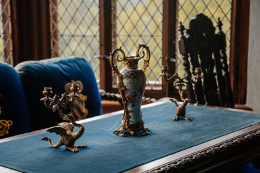 Castle interior. Candlesticks in the shape of a dragon, Chinese vase on a table covered with blue cloth against the window. Medieval castle Rozmberk nad Vltavou, Czech Republic, September 26, 2020 clipart