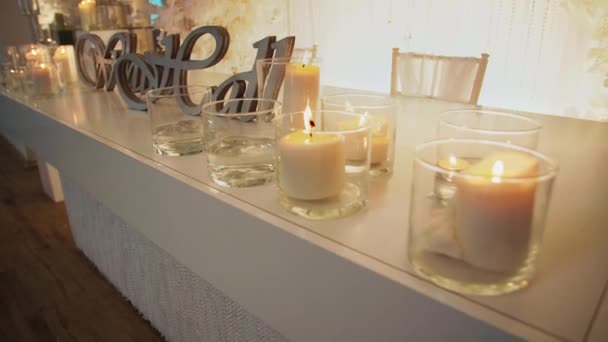 Горящие свечи, стоящие в стеклянной фляжке на столе с надписью "белый зал" — стоковое видео
