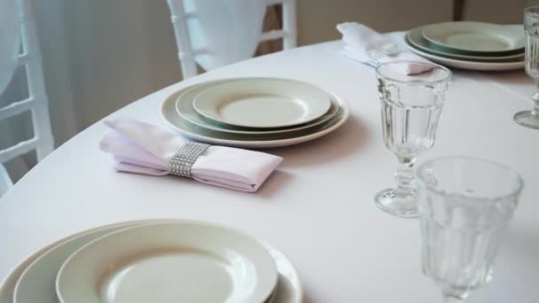 Ronde tafel met een wit tafellaken geserveerd platen wijn glazen en servetten — Stockvideo