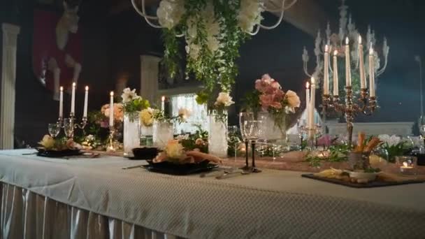 En tabell med svarta pilar med mat, vinglas, blomvaser, ljusstakar med ljus — Stockvideo