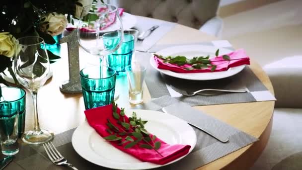 Un tavolo rotondo in legno decorato con composizioni floreali realizzate con piatti bianchi con tovaglioli rosa intorno ai quali sono presenti morbide sedie — Video Stock