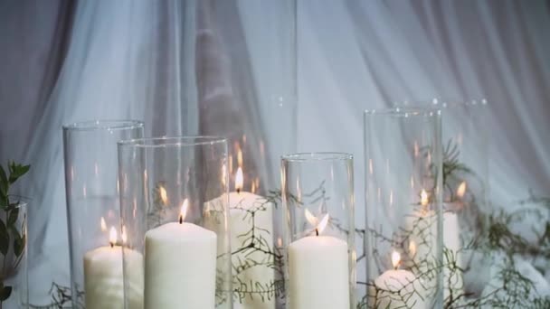 Dikke brandende kaarsen staande in transparante vazen omgeven door textiel — Stockvideo