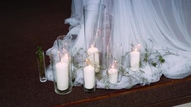 Dicke brennende Kerzen stehen in transparenten Vasen, umgeben von Textilien — Stockvideo