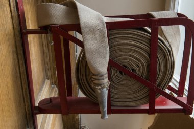 Eski bir gri yangın hortumu özel stand ahşap bir duvara bağlı yanmaz malzemeden yapılmış. Metalden yapılmış borular bağlanma.