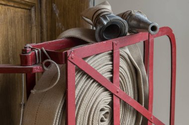 Eski bir gri yangın hortumu özel stand ahşap bir duvara bağlı yanmaz malzemeden yapılmış. Metalden yapılmış borular bağlanma.