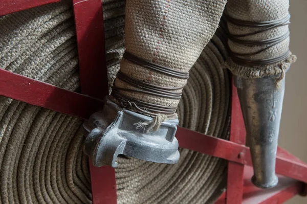 Eski bir gri yangın hortumu özel stand ahşap bir duvara bağlı yanmaz malzemeden yapılmış. Metalden yapılmış borular bağlanma.