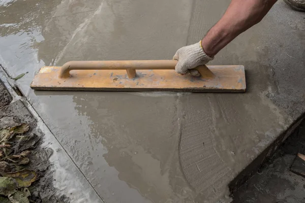Construction of a concrete walkway around a residential rural house in manual mode. Manually cooked mortar in a concrete mixer. Leveling the surface of the pavement with a special tool