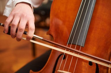 Çello çalan tanınmaz viyolonselcimiz. Çellist yay elinde. Doğrudan güneş ışığı