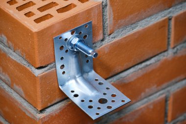 Stage of installation of a chemical anchor in a red building brick with cellular voids.  Fastening the metal angle on the bolt. clipart