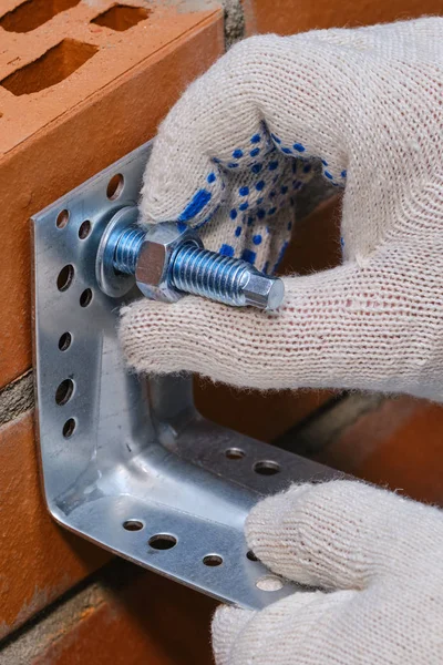 Stage of installation of a chemical anchor in a red building brick with cellular voids.  Fastening the metal angle on the bolt.