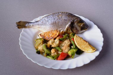 Örnek Restoran Paketi: Fırında Dorado balığı, iki kızarmış limon kamışı, haşlanmış domates, fasulye kabuğu ve beyaz tabakta Brüksel lahanası.