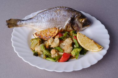 Örnek Restoran Paketi: Fırında Dorado balığı, iki kızarmış limon kamışı, haşlanmış domates, fasulye kabuğu ve beyaz tabakta Brüksel lahanası.