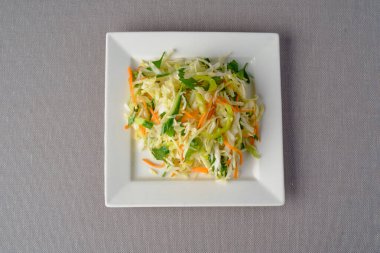 Ana malzemelerle birlikte taze pişirilmiş sebze salatası: lahana, salatalık, havuç, maydanoz, beyaz kare tabakta sunum olarak sunulan ayçiçeği yağı.