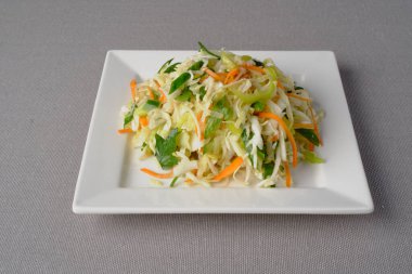 Ana malzemelerle birlikte taze pişirilmiş sebze salatası: lahana, salatalık, havuç, maydanoz, beyaz kare tabakta sunum olarak sunulan ayçiçeği yağı.