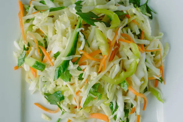 Ana malzemelerle birlikte taze pişirilmiş sebze salatası: lahana, salatalık, havuç, maydanoz, beyaz kare tabakta sunum olarak sunulan ayçiçeği yağı.