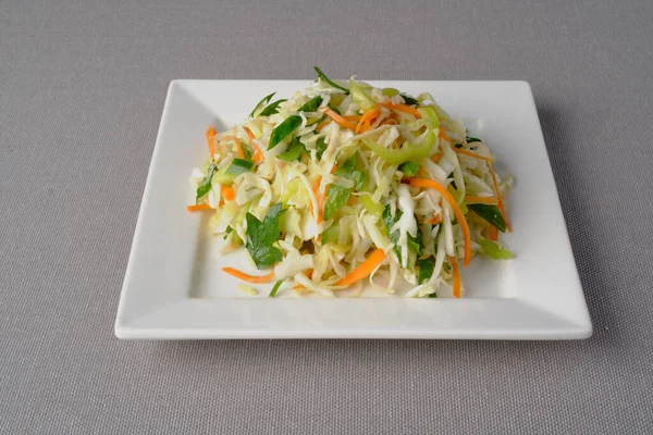 Ana malzemelerle birlikte taze pişirilmiş sebze salatası: lahana, salatalık, havuç, maydanoz, beyaz kare tabakta sunum olarak sunulan ayçiçeği yağı.