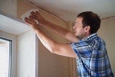 35-40 yaşlarında, normal mavi ekose gömlekli bir adam tek başına bir apartman dairesinin duvarına duvar kağıdı yapıştırıyor. Aletlerin elinde, yapıştırıcı sürmek için bir silindir. Ölçüm ve hizalama süreci