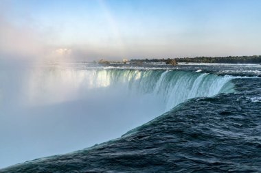 Niagara Falls, bulutlar su sis ve açık mavi su, arka planda yeşil orman ile yakından görmek