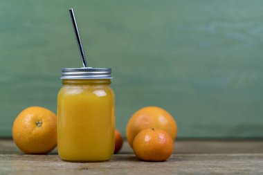 Şeffaf mason cam portakal suyu ile veya bir saman, portakal ve mandalina, kokteyl yeşil duvar arka plan kopya alanı ile karşı taraftan görüntülendi?