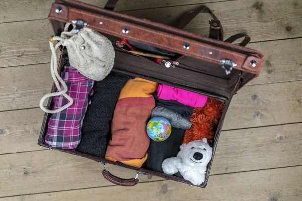 Open vintage suitcase of brown leather packed for the journey with rolled clothes, globe and polar bear toy as a mascot. Case is on the floor and viewed from above