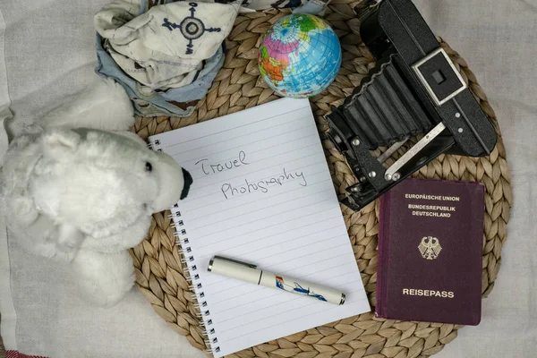 Travel plans concept with list in notebook sheet, among different objects symbolising traveling theme, such as passport, globe, old photo camera and polar bear mascot toy