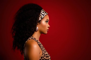 Leopar desenli üst ve saç bandı takan şık genç bir model, kırmızı bir arka plana karşı poz veriyor, lüks güzellik ve güveni ön plana çıkarıyor..