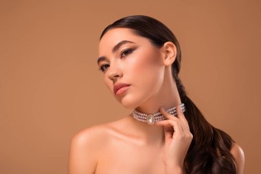 Zarif mücevherler takan güzel esmer bir kadının zarif yakın çekimi yumuşak bir bej arka planda kusursuz cilt rengini vurguluyor..