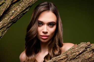 Çekici bir kadın modelin şık bir portresi. Koyu yeşil bir arka planda desenli ağaç kabuğuyla kusursuz şekillendirilmiş gür kahverengi saçları var..