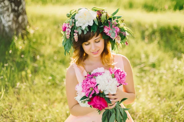 幸せな笑みを浮かべて少女花の花輪と日当たりの良い夏の日にシャクヤクの花束 — ストック写真