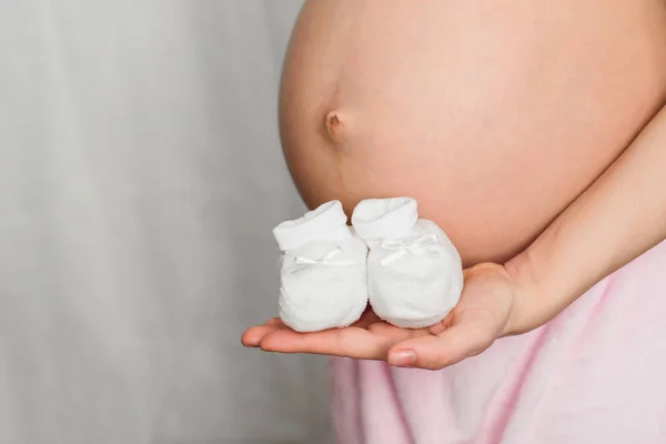Mani di una donna incinta con stivaletti per un neonato — Foto Stock