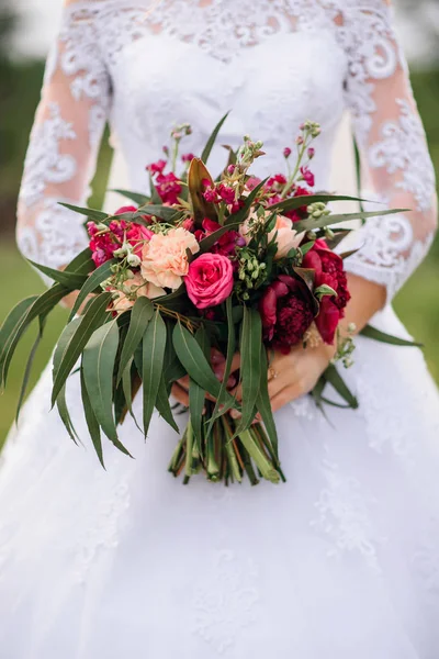 Svatební kytice s pivoňky červené a zelené listy v rukou nevěsty — Stock fotografie